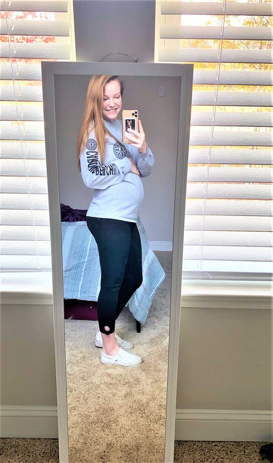 Mirror selfie of pregnant woman holding her baby bump 