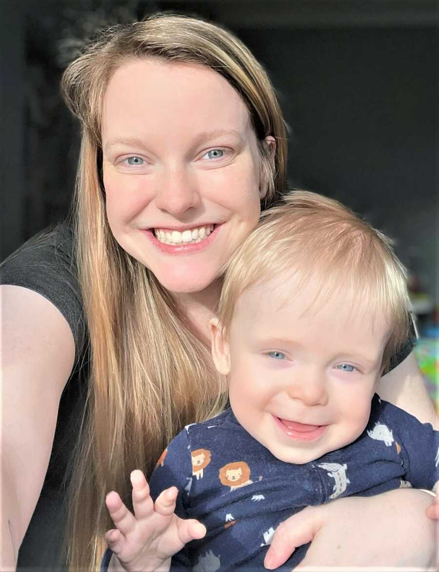 selfie of a mom with her toddler son sitting on her lap while they both smile at the camera 