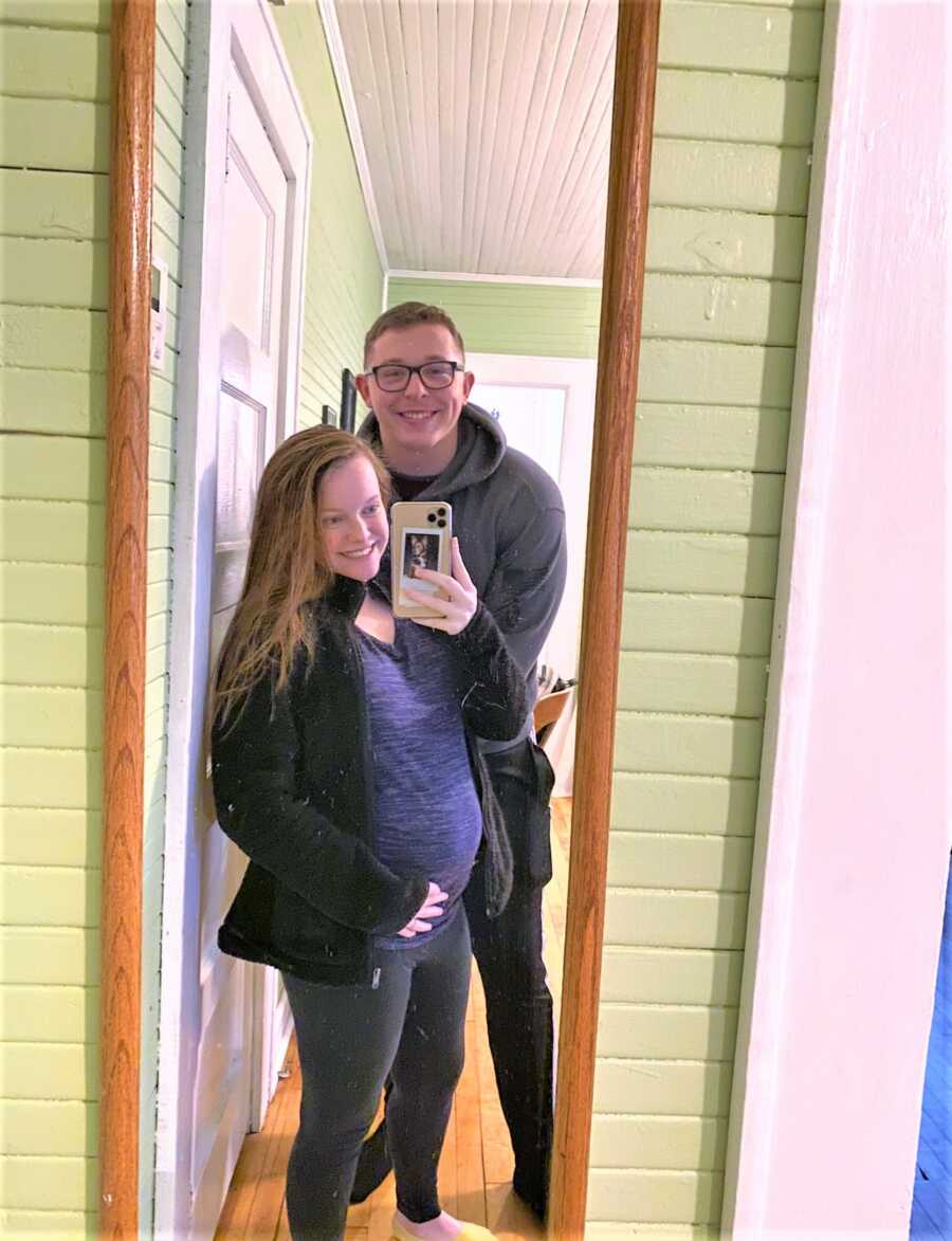 mirror selfie of pregnant woman standing next to her husband 