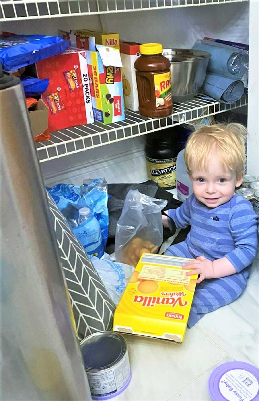 toddler boy sneaking into the food pantry and holding a box of cookies