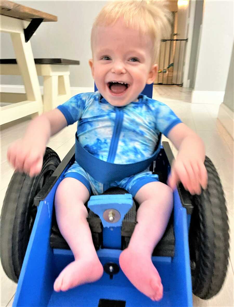 baby boy looking excited while moving the wheels of his wheelchair 