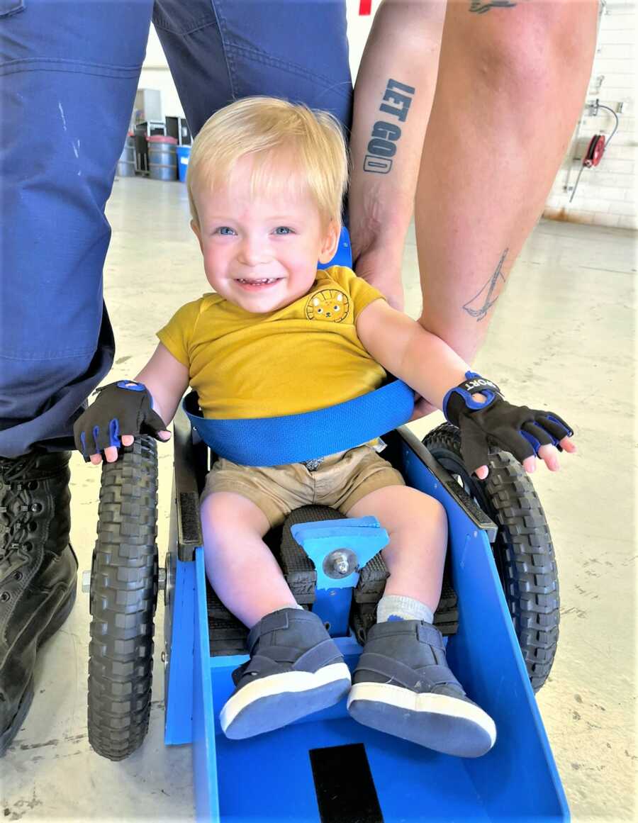 Baby boy sitting on special wheelchair and smiling