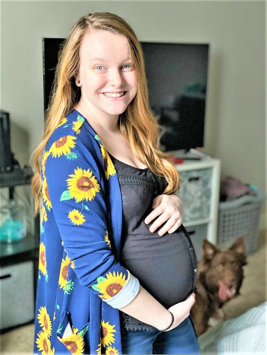 Pregnant woman holding her big baby bump with her dog on the background