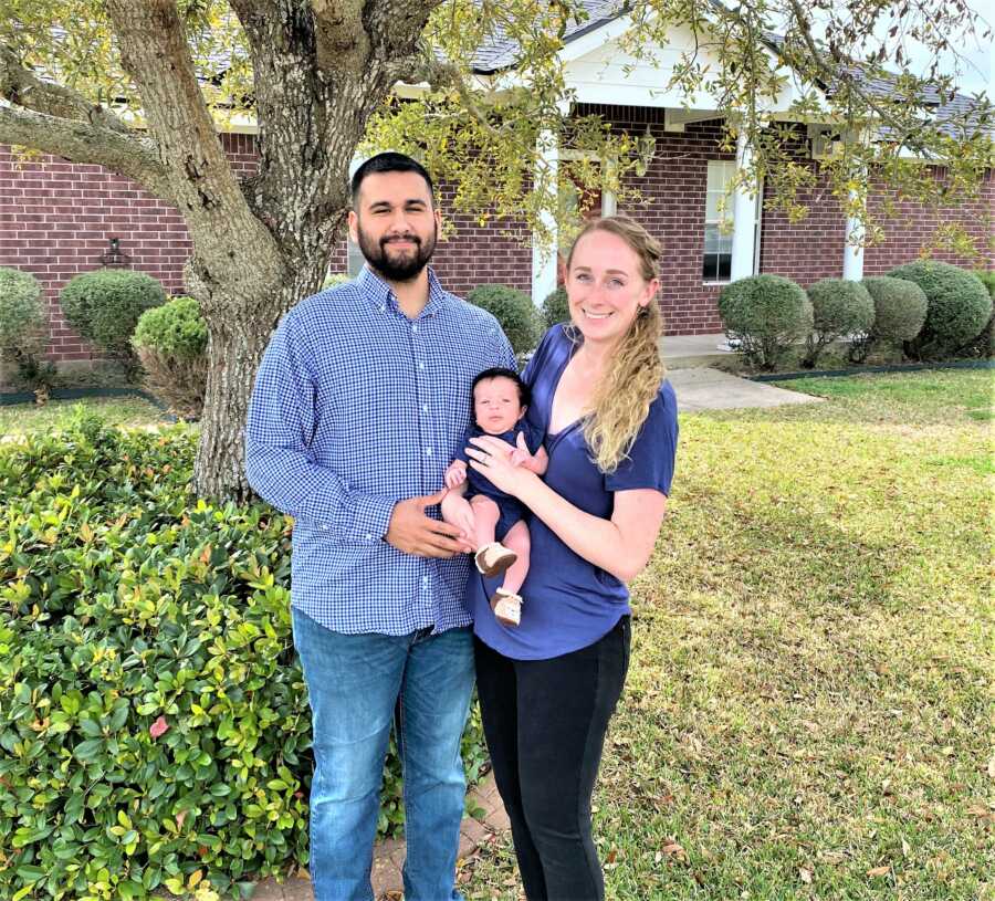 Mom and dad holding their newborn son while standing in front of a house