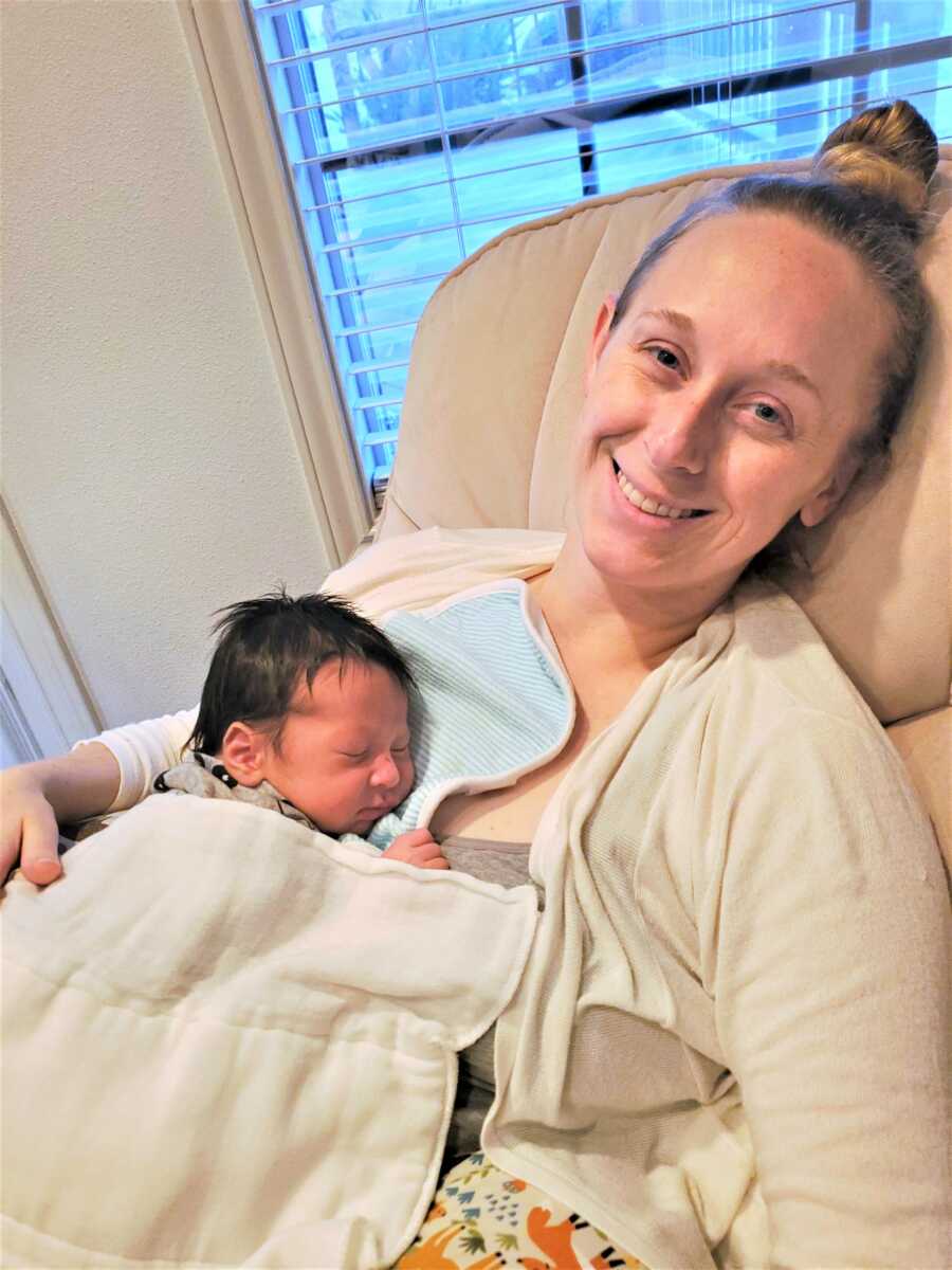 Postpartum mom resting on a couch with her newborn son sleeping on her shoulder 