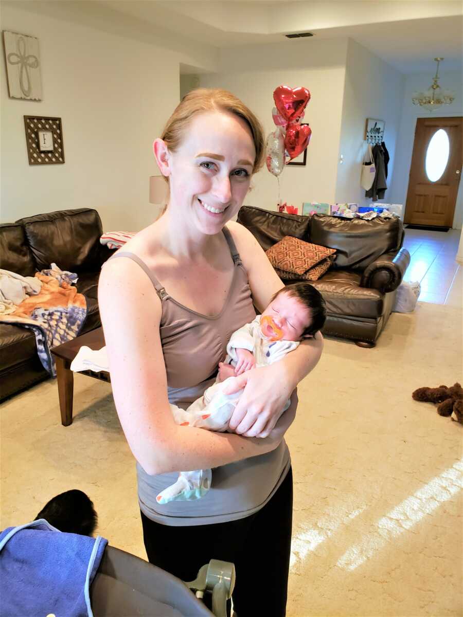 Postpartum mom holding her newborn son in her arms while standing smiling in the Livingroom of their home