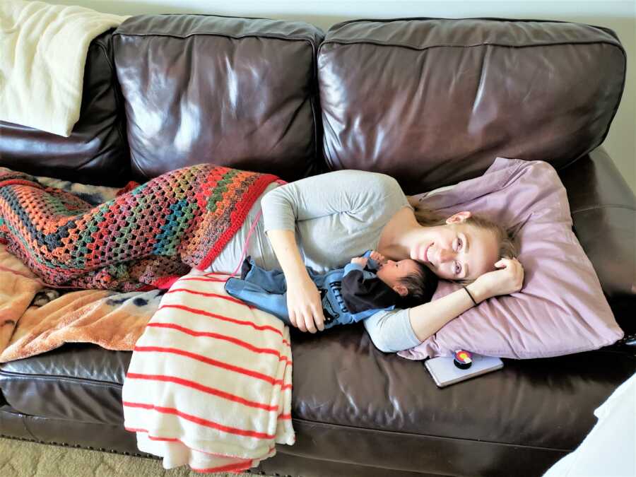 Mom laying on a couch next to her sleeping newborn son