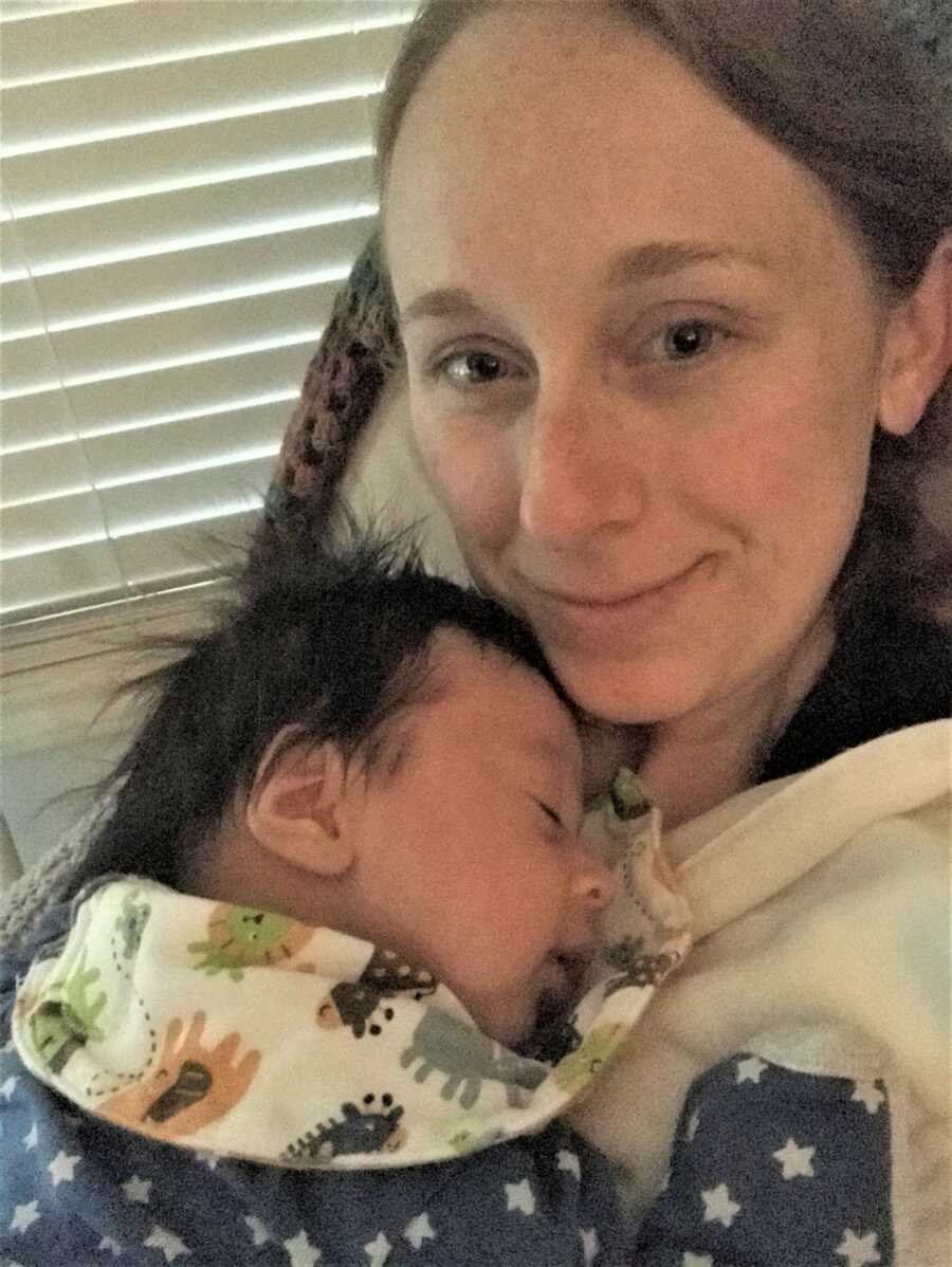 selfie of a mom sitting on a couch with her newborn son resting on her chest