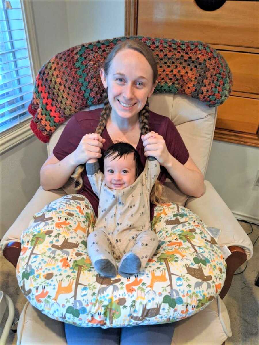 Mom sitting on a couch holding up the arms of her baby son who is sitting on her lap