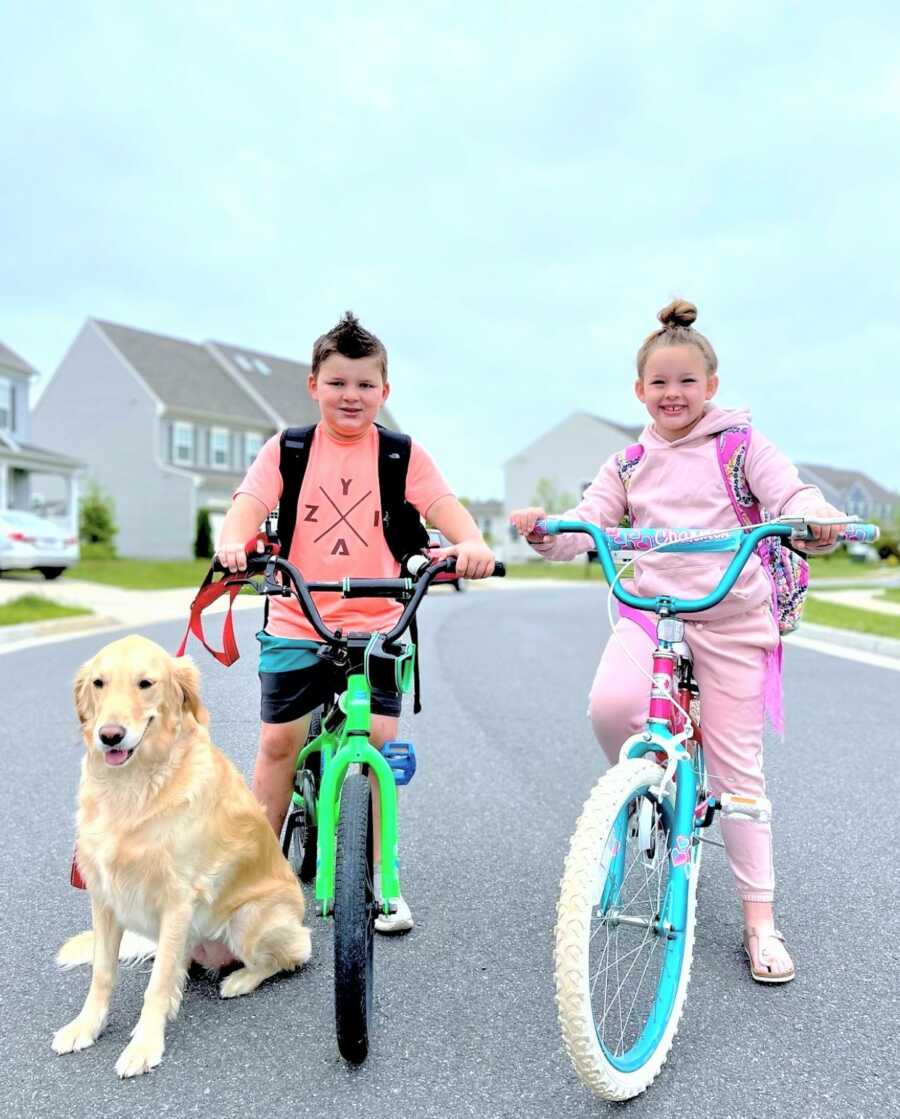 brother and sister riding bikes around the neighborhood next to their golden retriever dog 