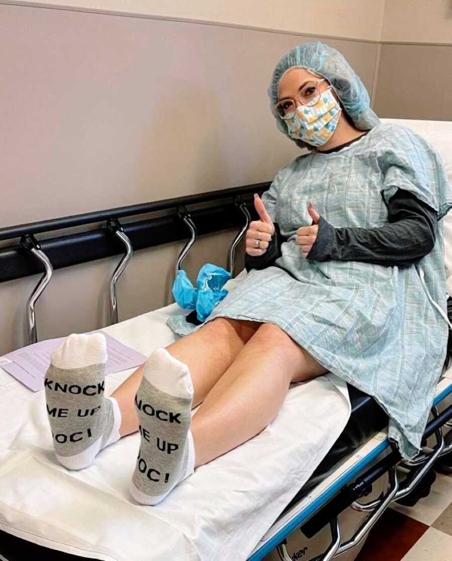 Woman undergoing IVF takes a photo in surgical gear with socks that read "knock me up doc!"