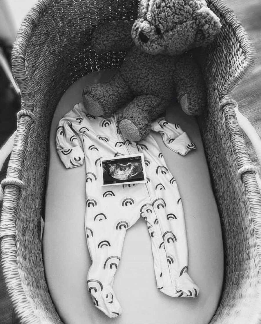 Woman takes a photo of an ultrasound photo with a rainbow onesie in a crib