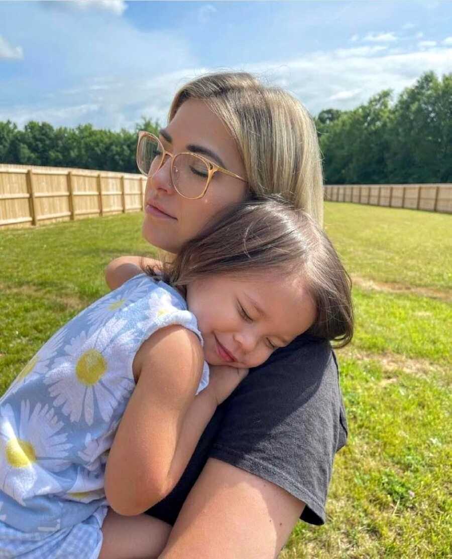 Mom cuddles with adoptive daughter while they enjoy the sunshine together