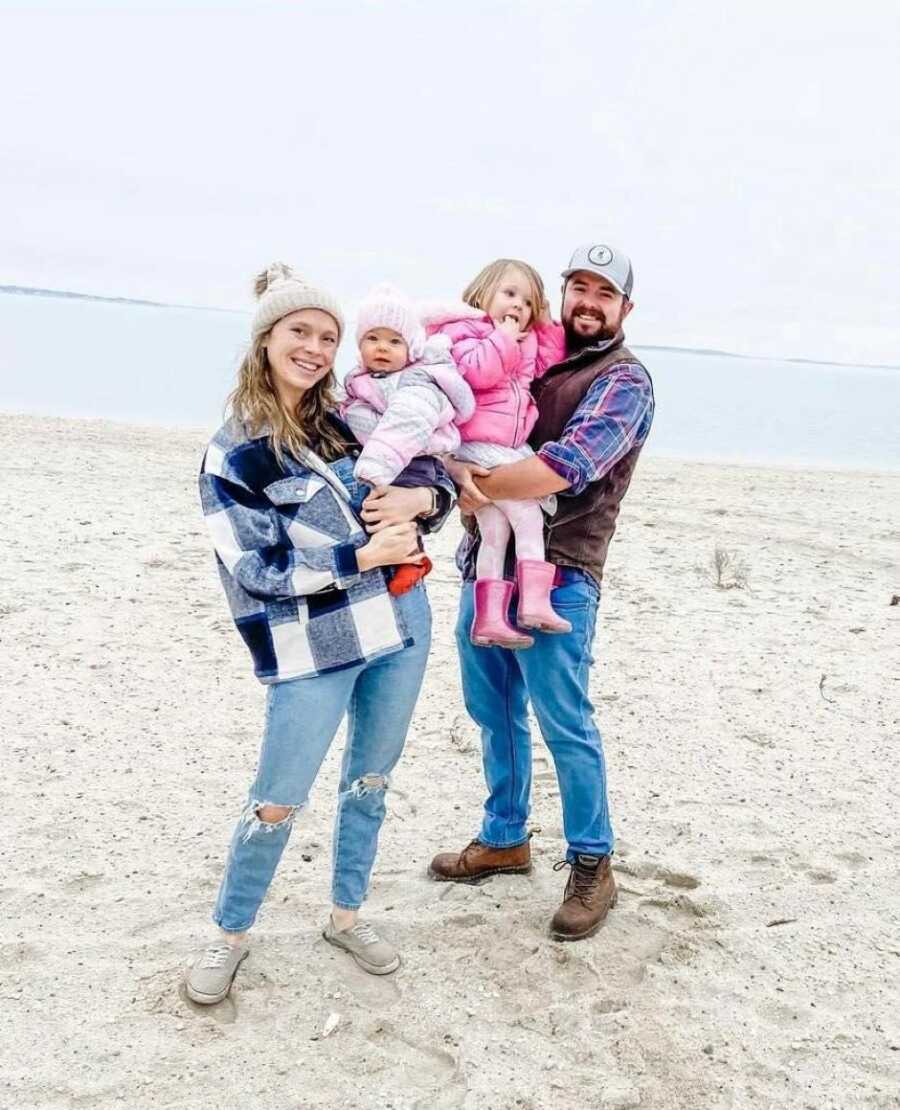 Family of four take group photo on the beach in jackets and hats
