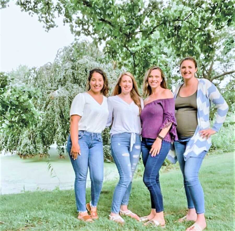 group of 4 women standing closely next to each other smiling at a nature park 