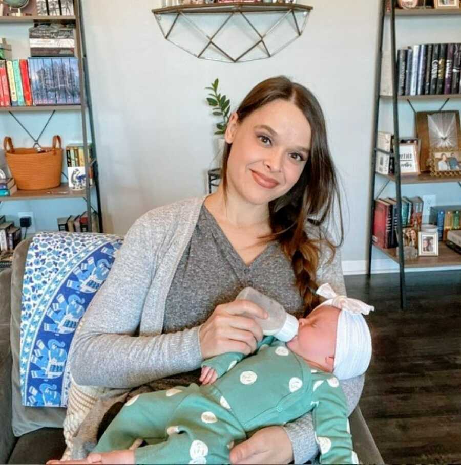 Woman smiles for a photo while bottle-feeding her newborn daughter