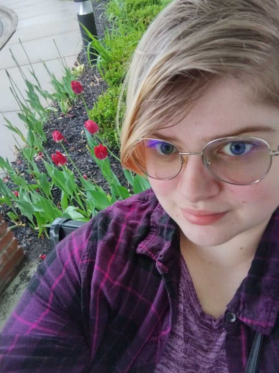 non binary person taking a selfie in front of flowers