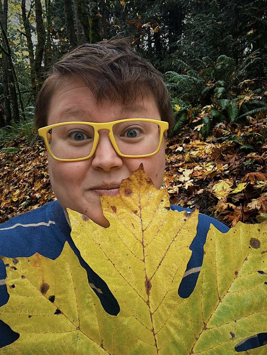 non binary person holding up a giant leaf