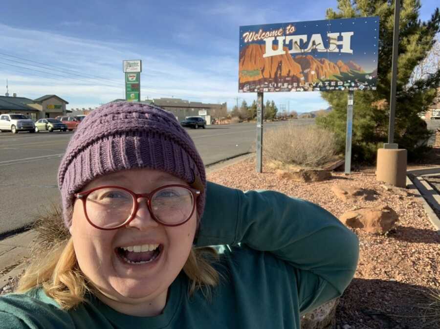 non binary person in front of a state sign
