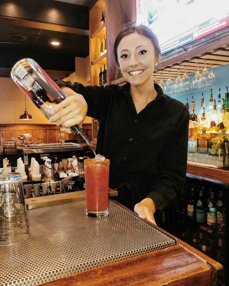 Bartender smiles for a photo while making someone a cocktail