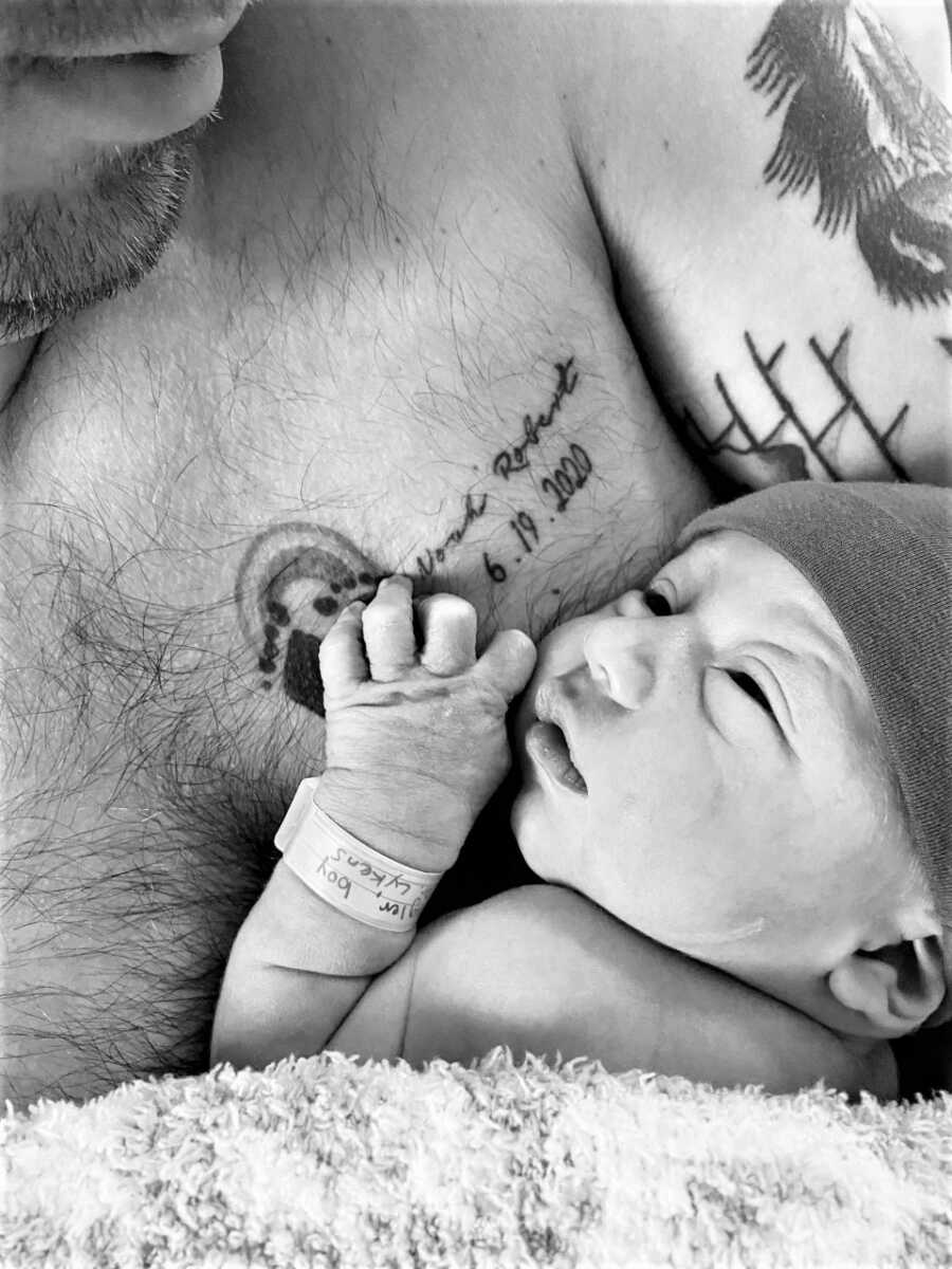 Dad holding newborn baby son on his bare chest with a tattoo of the footprints of his stillborn baby son