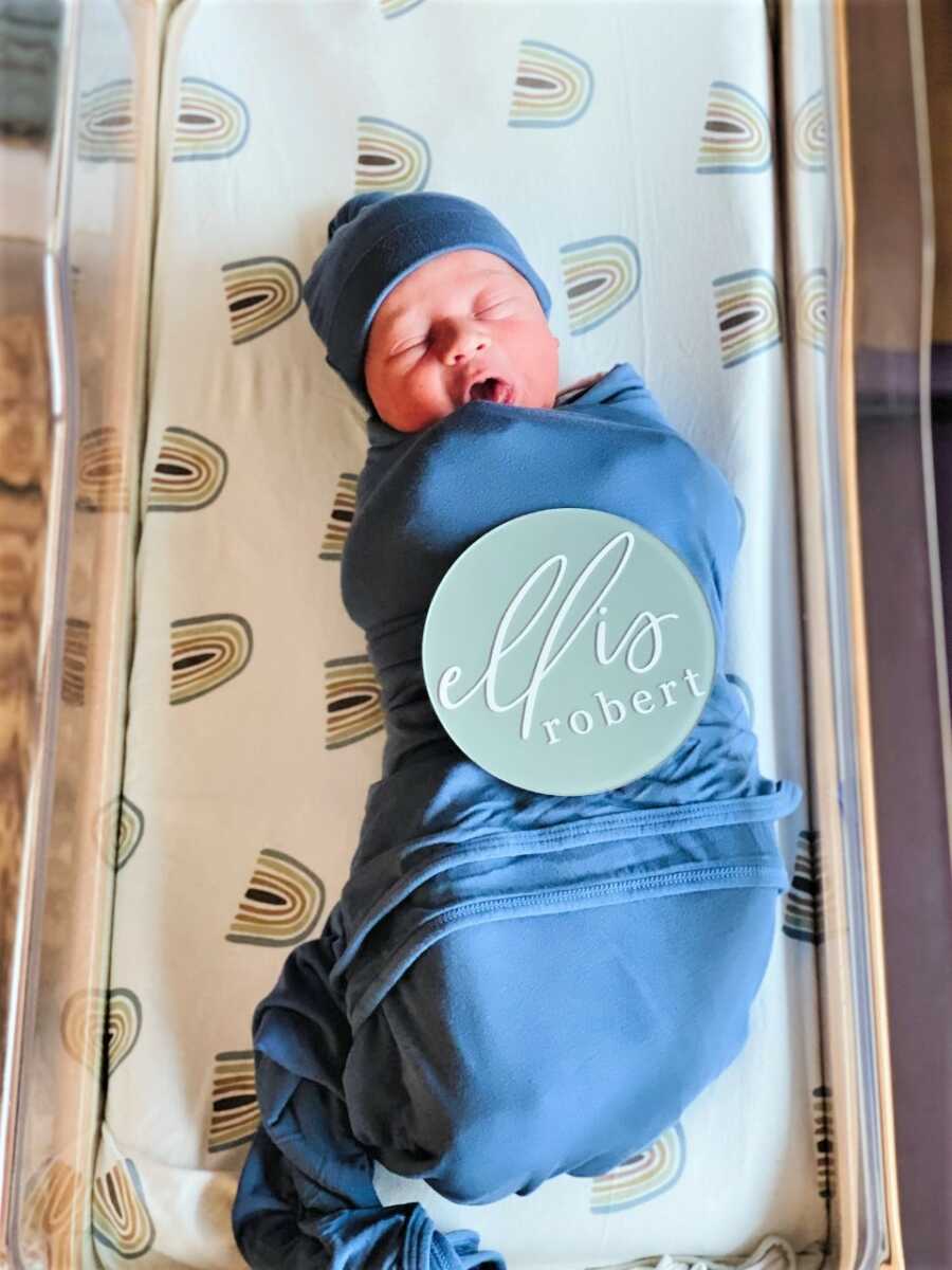 Newborn baby son laying on a bed with rainbow sheets 