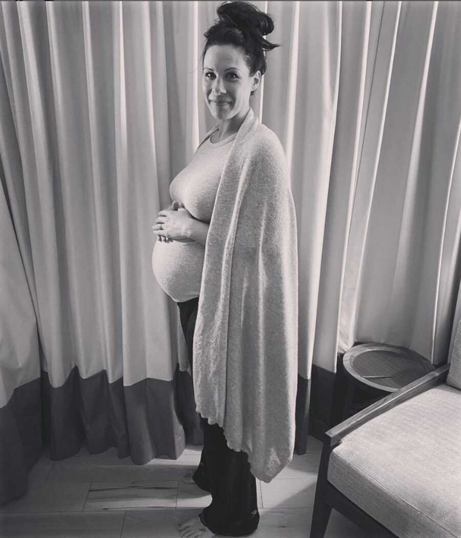Smiling pregnant woman standing with hands on her stomach 
