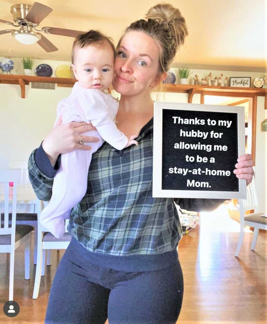 stay at home mom holding her baby and a letter sign thanking her husband for allowing her to be a stay-at-home mom