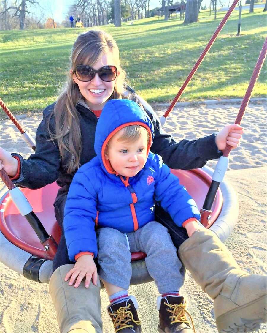 Mom and her toddler son sitting on a swing at a playground 