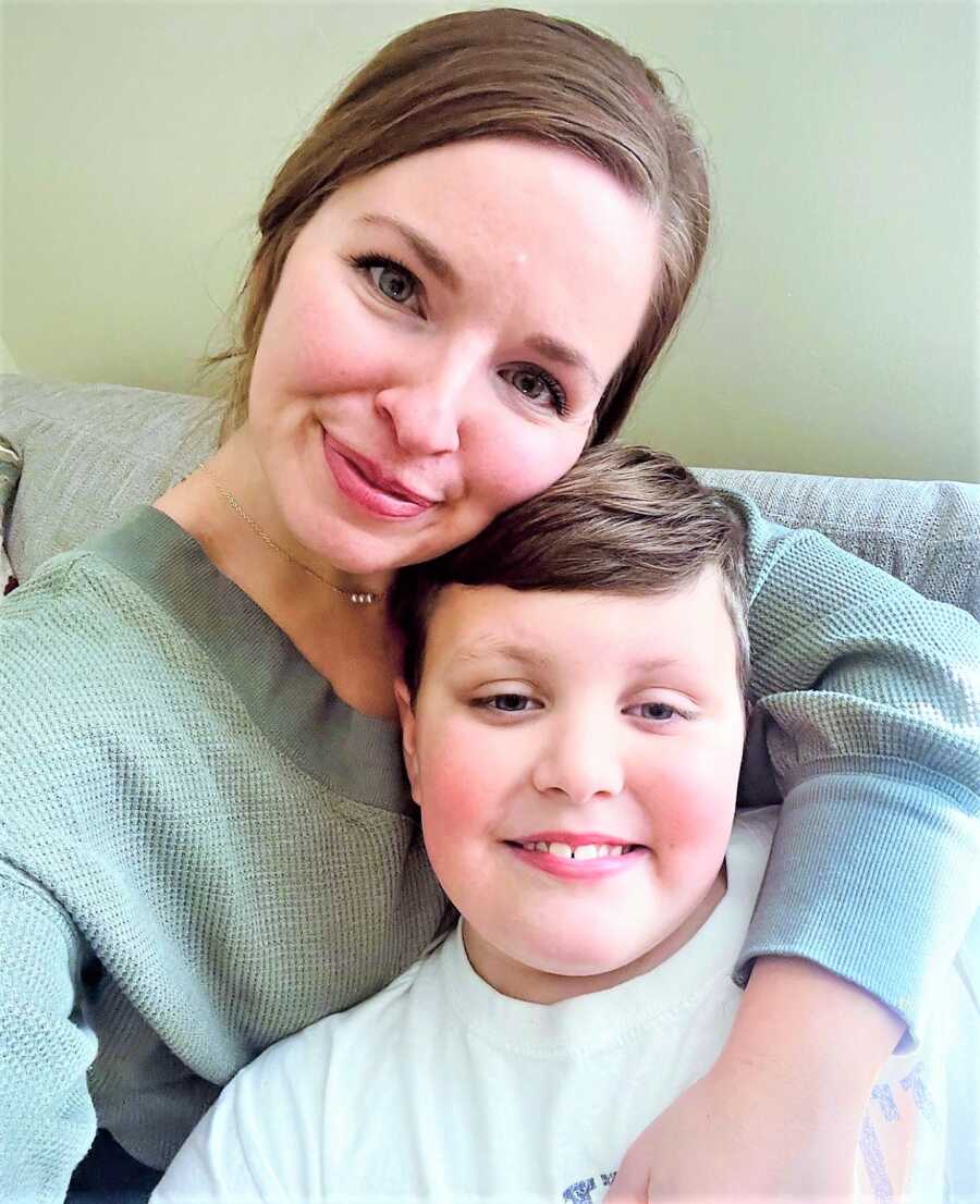 selfie of a mom with her son resting his head on her shoulder while they both sit on a couch 