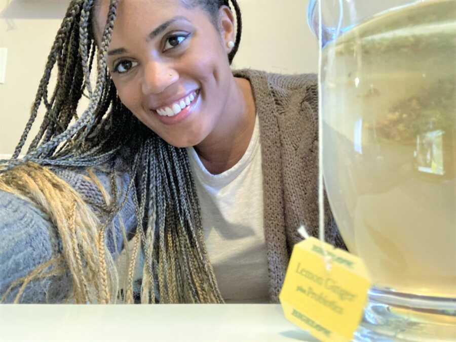 selfie of a black woman with long braided hair with a cup of hot tea