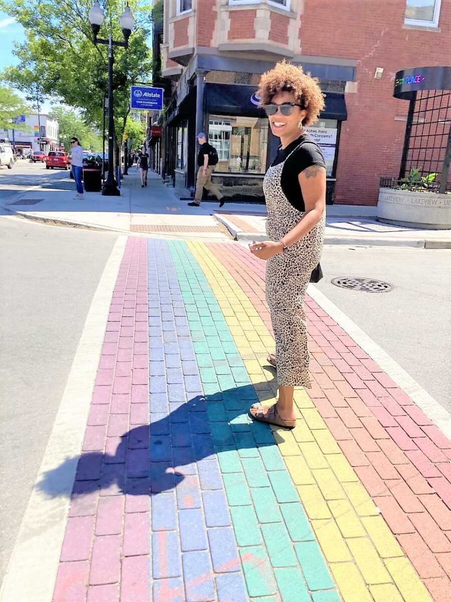 Black lesbian woman walking on a pedestrian crossing painted like a rainbow 