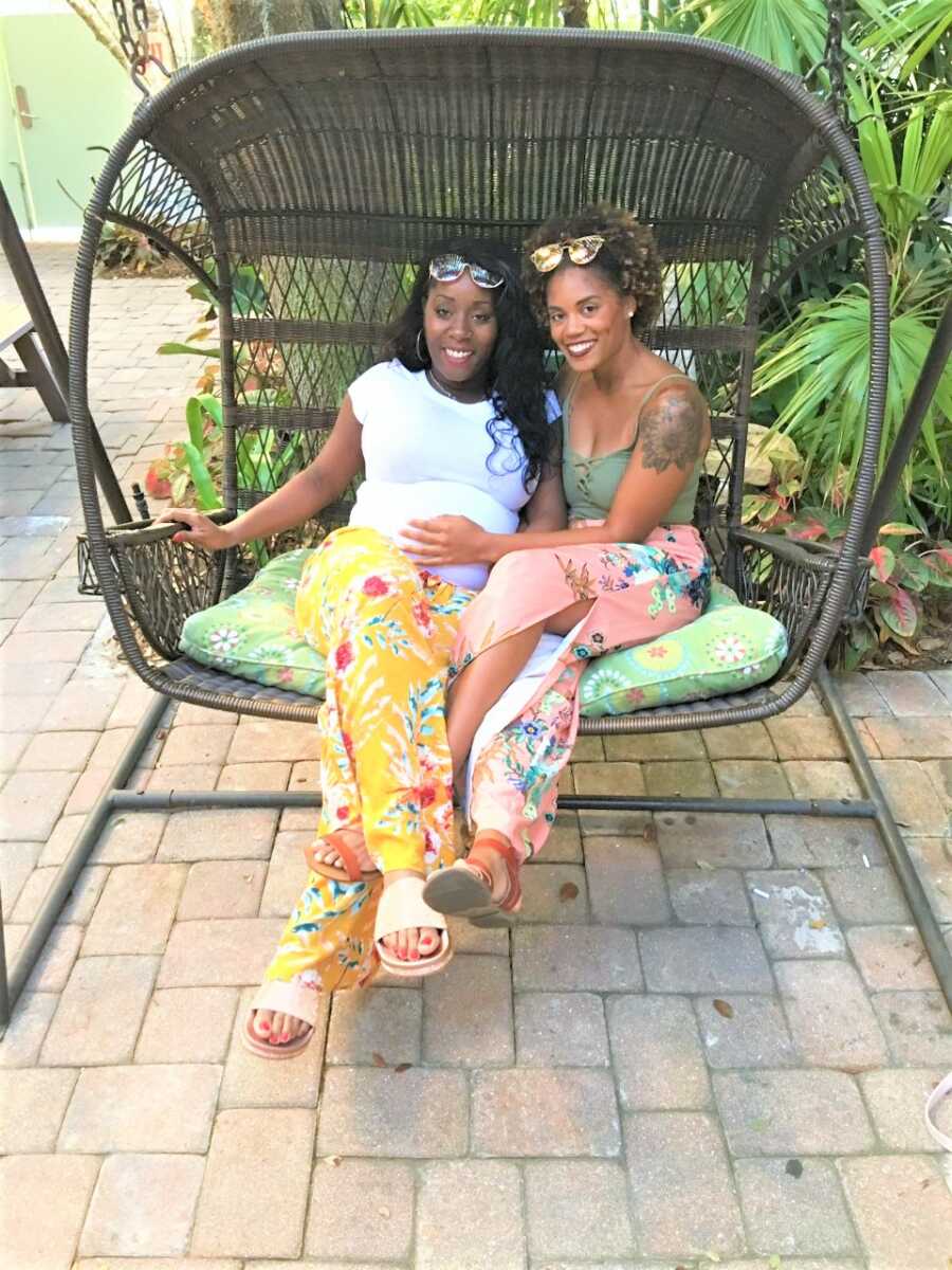 Black twin sisters sitting on a big patio chair 