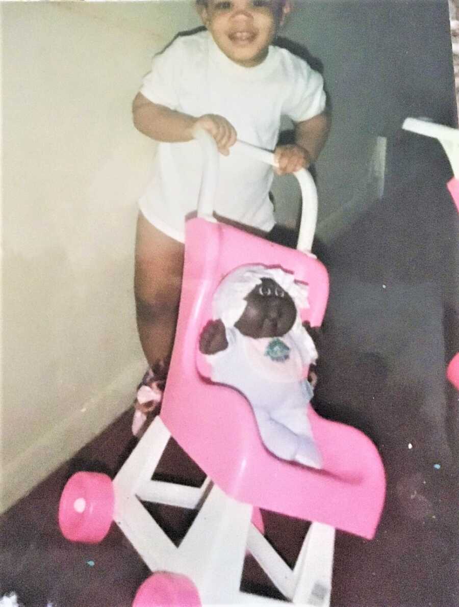 Little black girl playing with a black baby doll in a pink baby stroller 