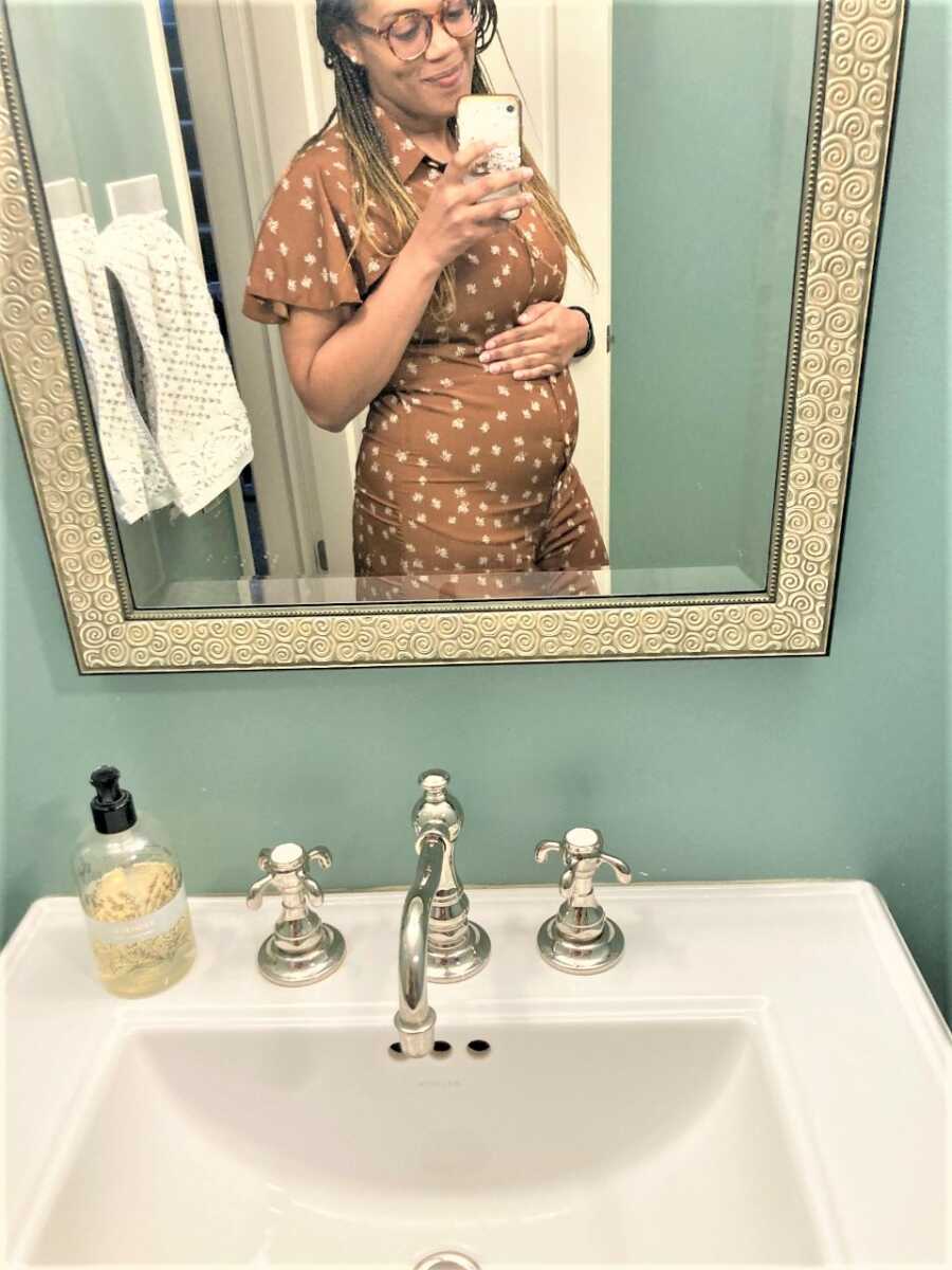 Mirror selfie of pregnant woman holding her belly