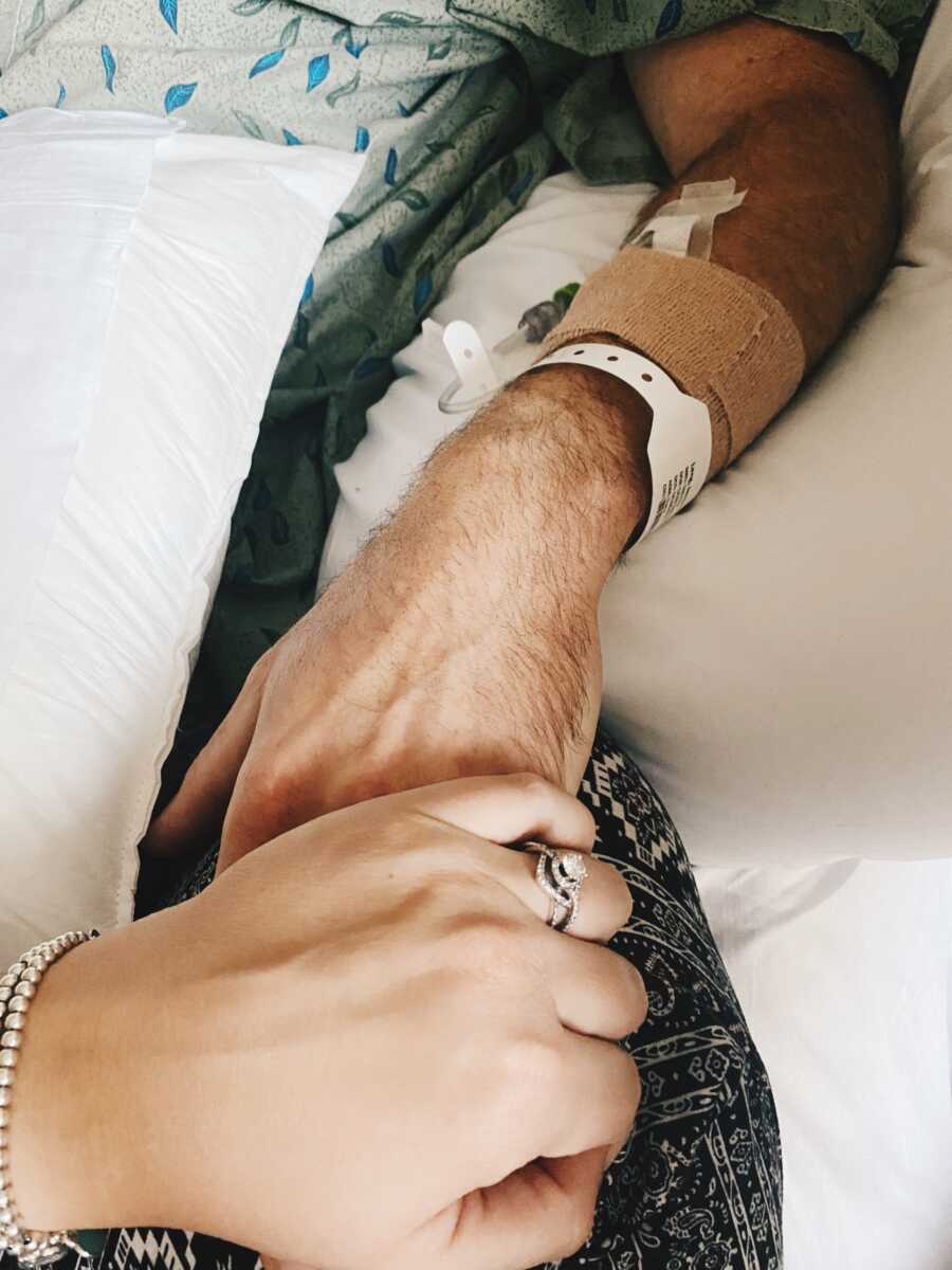 wife holding husband's hand while he is in the hospital