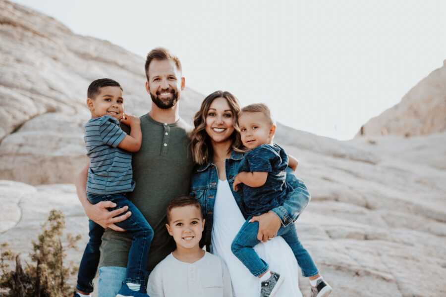 A family of five stand together in front of a rock structure