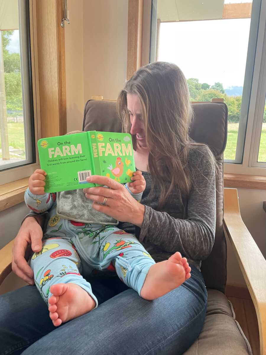 Foster mom holds baby on her lap in a rocking chair and reads a book.