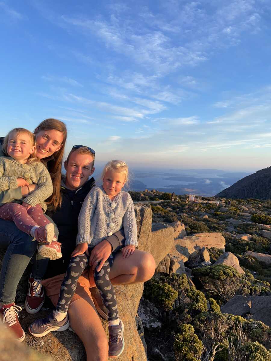 Foster family takes picture together with beautiful landscape and sunset behind them.