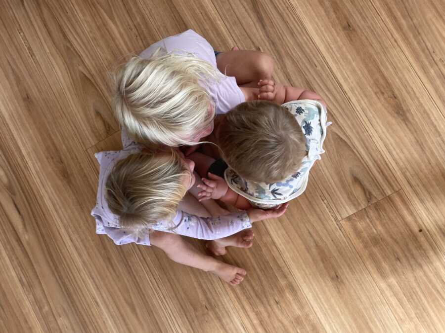 Top view of three young siblings hugging each other as they sit on the floor.