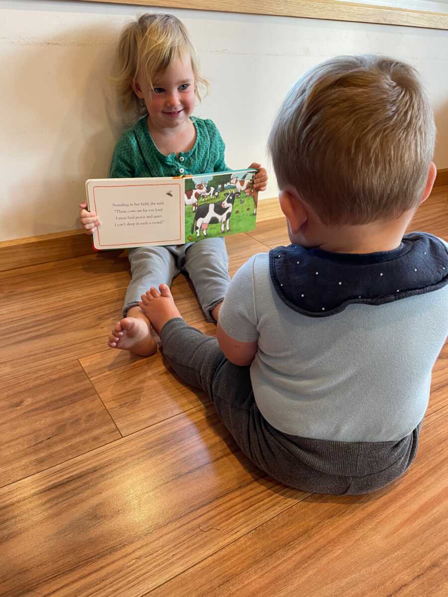 Sister holds up book as she reads to younger brother.