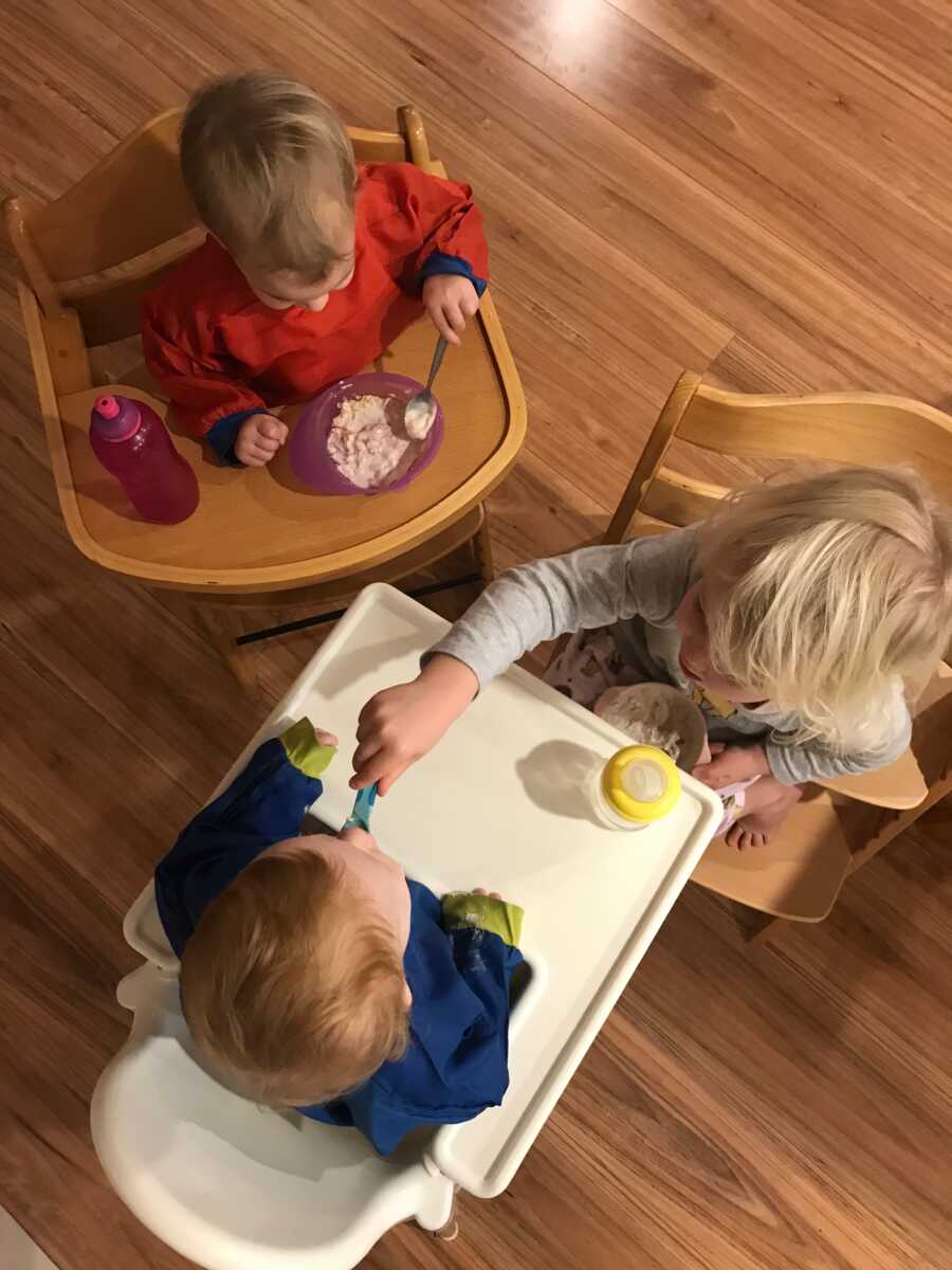 Young foster siblings sit in highchairs next to biological daughter.