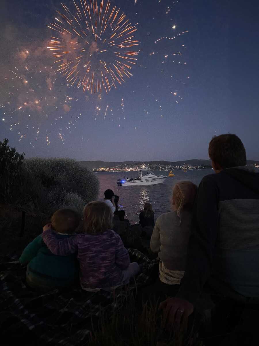 Family sits in the dark and watches fireworks over the lake.