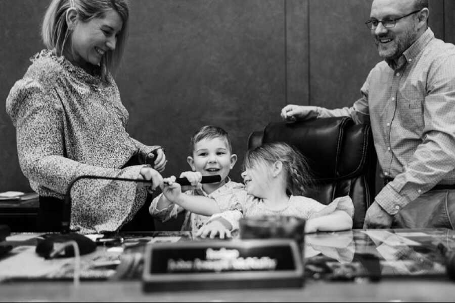 Newly adopted siblings sit in judge's chair in court room.