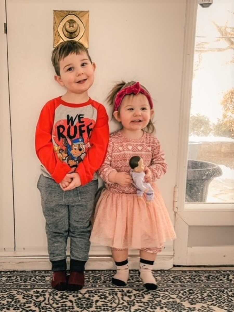 Siblings in foster care stand side by side in front of door, wearing red and pink outfits.