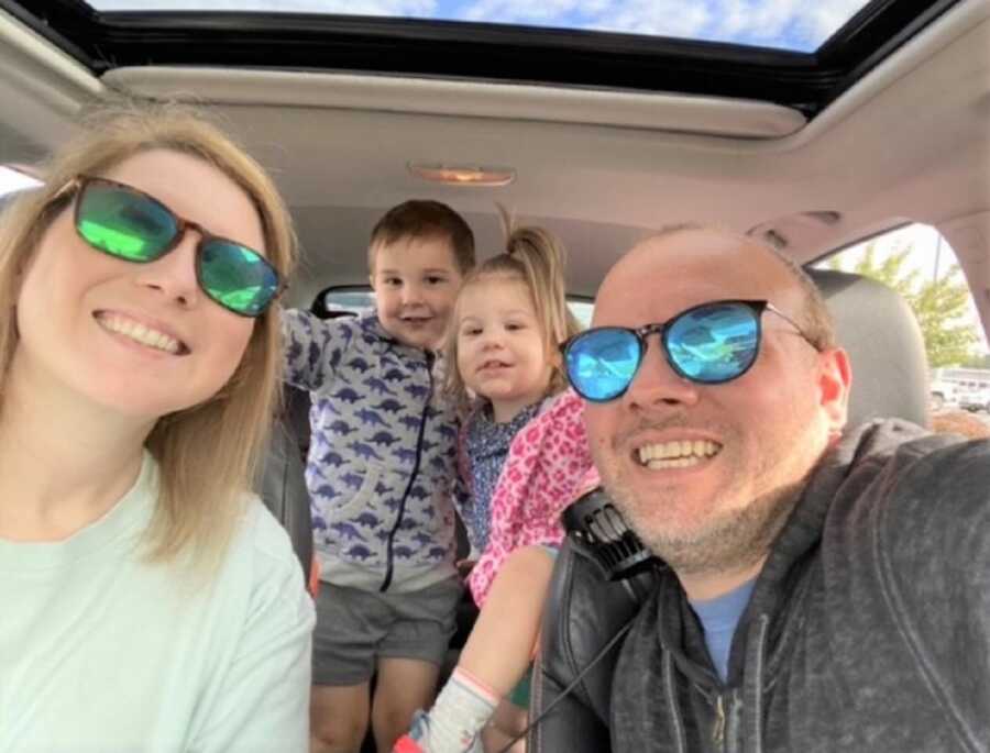 Foster parents take selfie in the car with two foster children in the back seat.