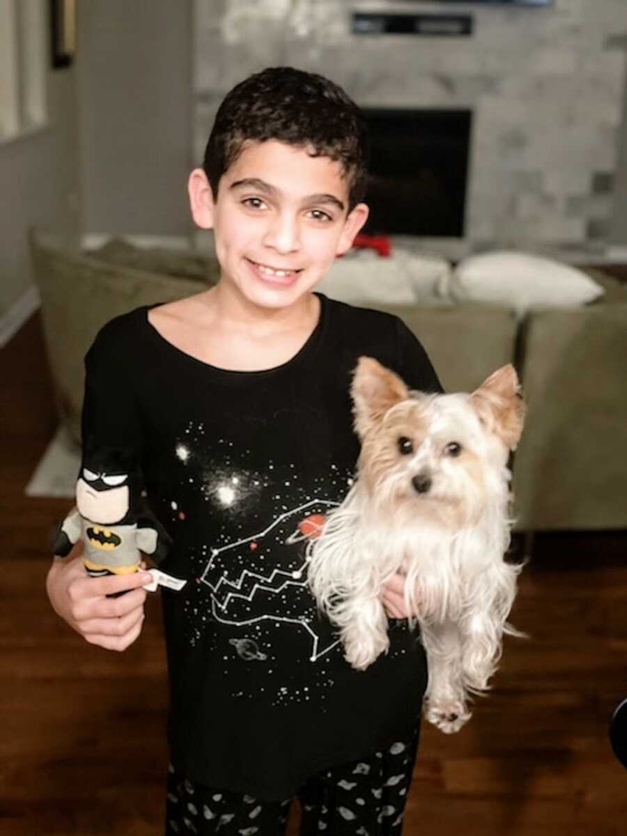 A young autistic boy holds his dog and a toy