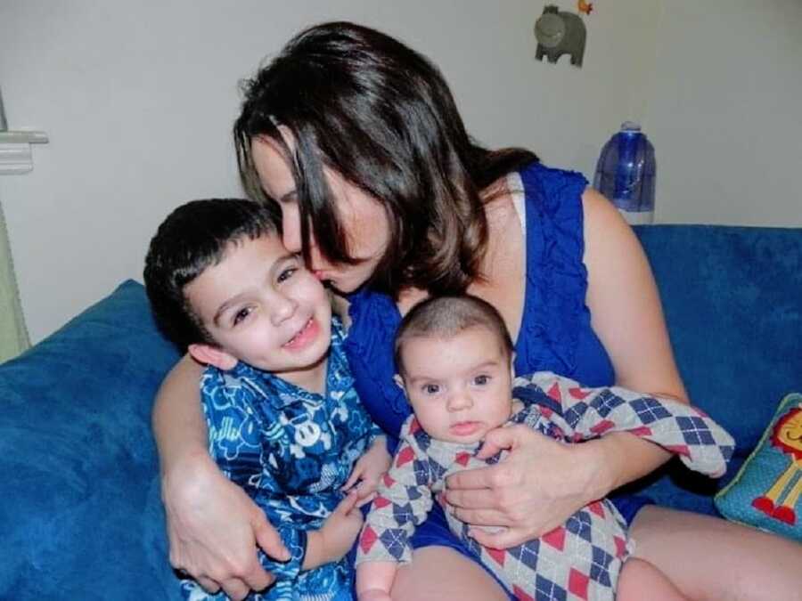 A mom holds her two sons and kisses one of them on the head