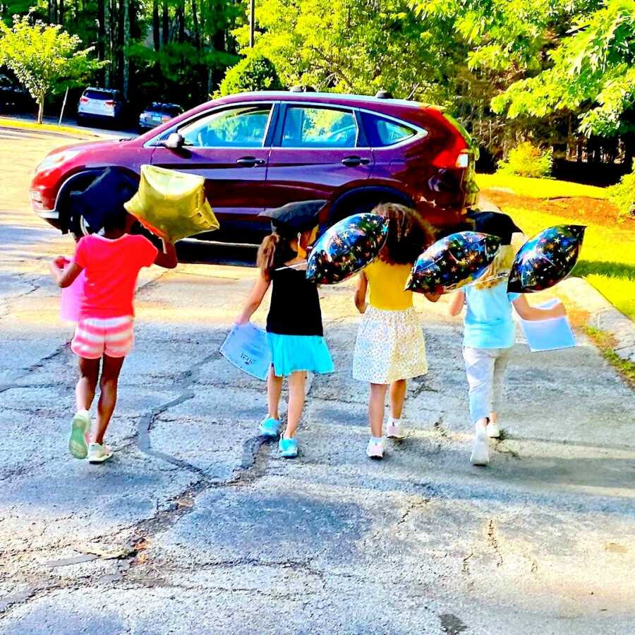 four preschool friends walk together in graduation caps with graduation balloons