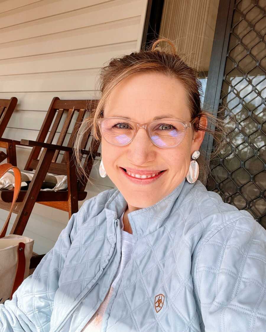 A mom sitting on a bench on her porch wearing a blue jacket